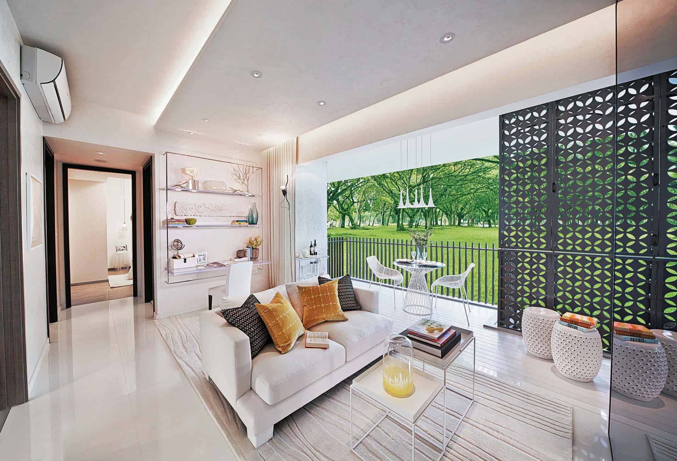 Bright and modern living space at The Inflora featuring a white sofa with colorful cushions, sleek built-in shelves, and a stylish workspace. The room opens up to a spacious balcony with a dining set and decorative screens, offering a lush green view of a tree-lined field, blending indoor comfort with outdoor serenity.
