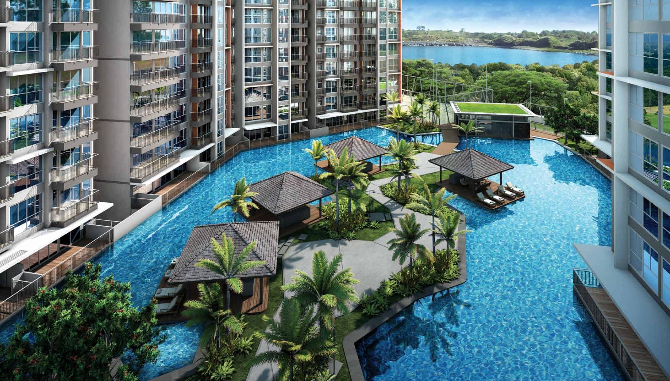Aerial view of the lagoon-style swimming pool at Qbay Residences, featuring poolside cabanas, lush palm landscaping, and high-rise residential blocks surrounding the water, with a scenic view of the waterway and greenery in the background.