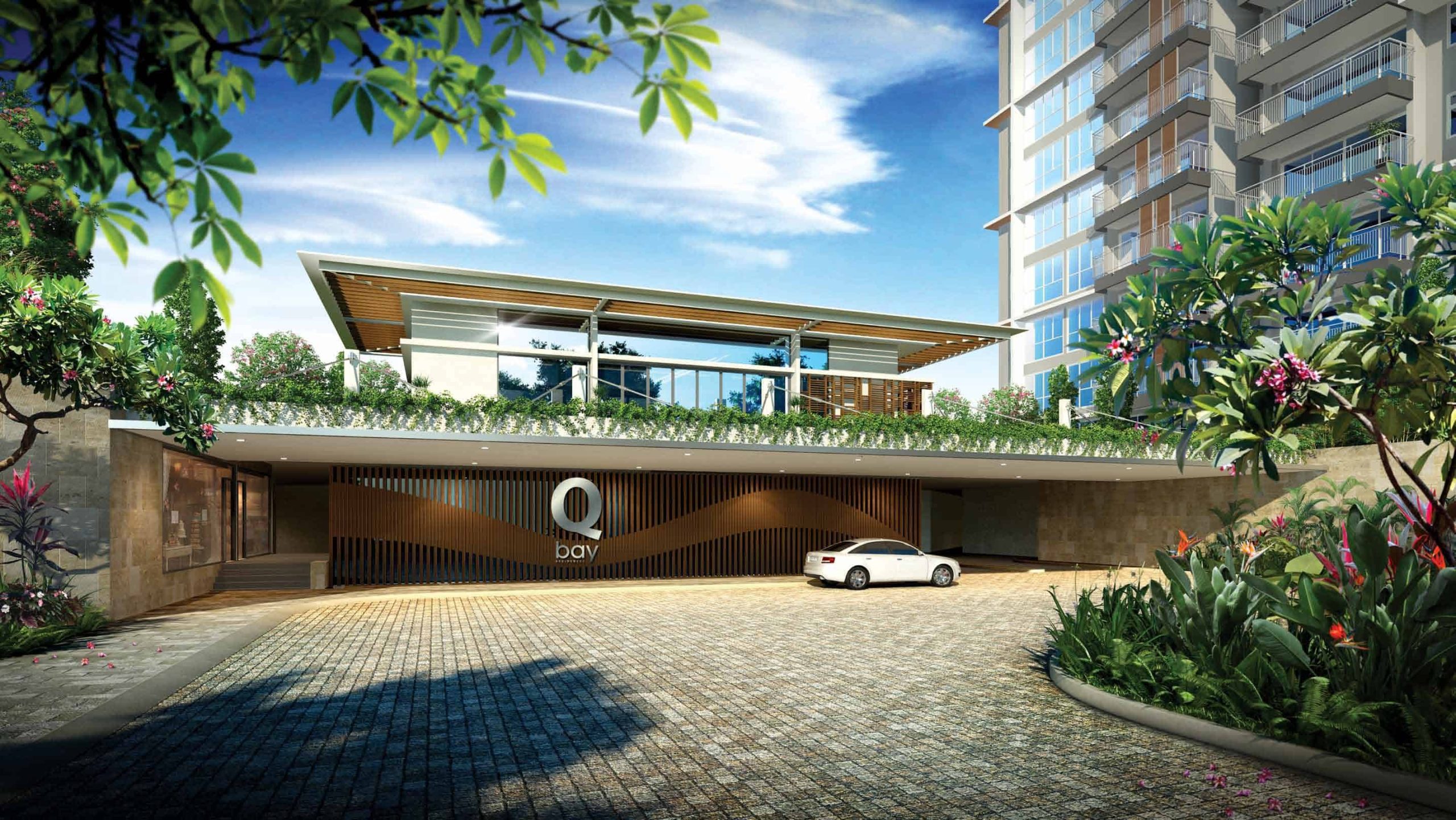 Entrance view of Qbay Residences featuring a modern drop-off area with a white car, sleek architectural design, and landscaped greenery, set against the backdrop of residential towers and a bright blue sky.