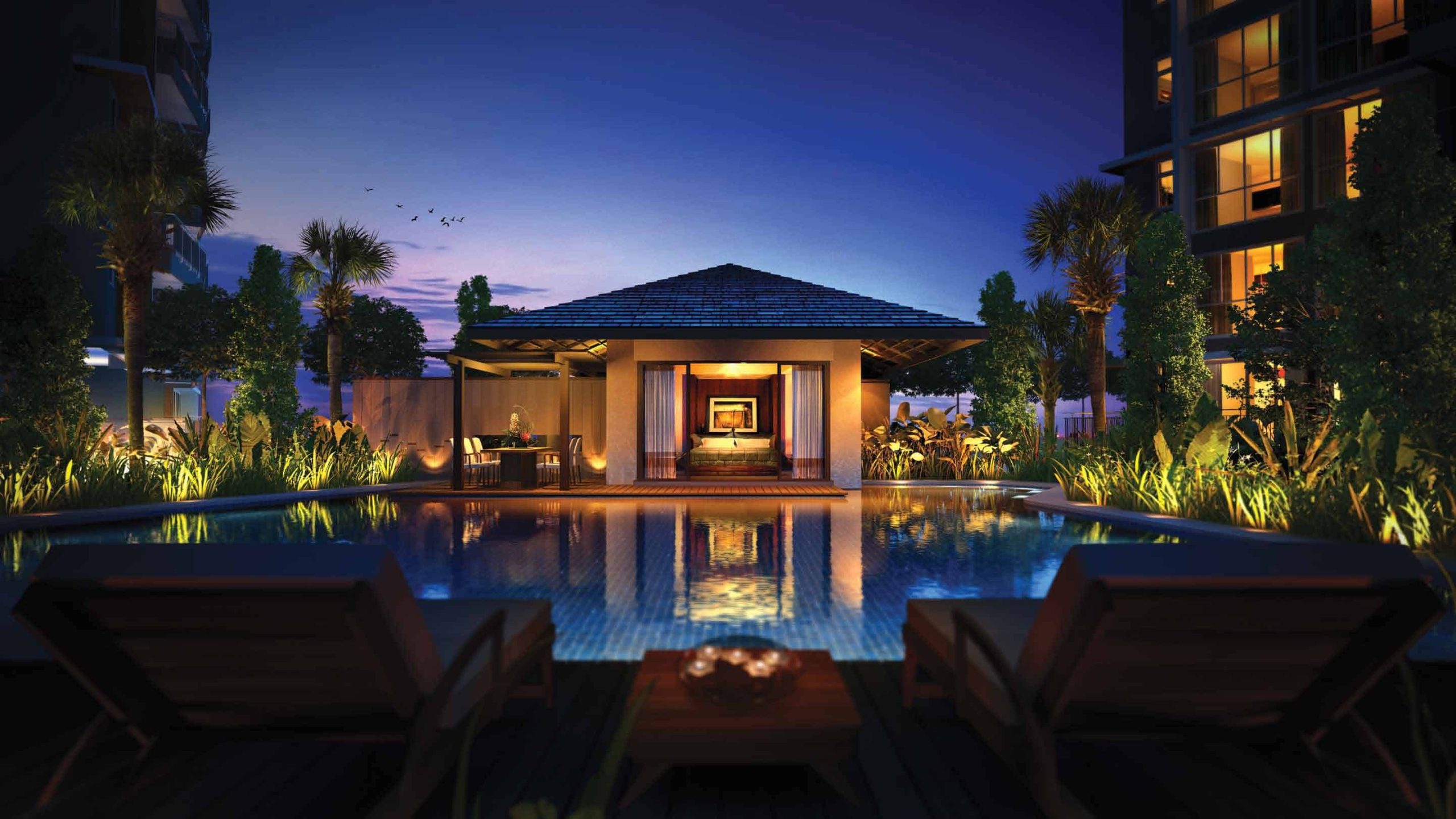 Night view of a tranquil poolside pavilion at Qbay Residences, featuring warm ambient lighting, lush landscaped surroundings, and sun loungers facing a luxurious cabana reflected in the still waters of the swimming pool.
